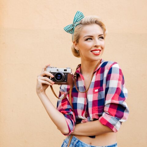 Beautiful cheerful pinup girl in yellow dress using vintage camera