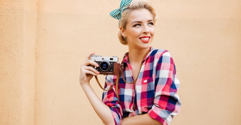 Beautiful cheerful pinup girl in yellow dress using vintage camera